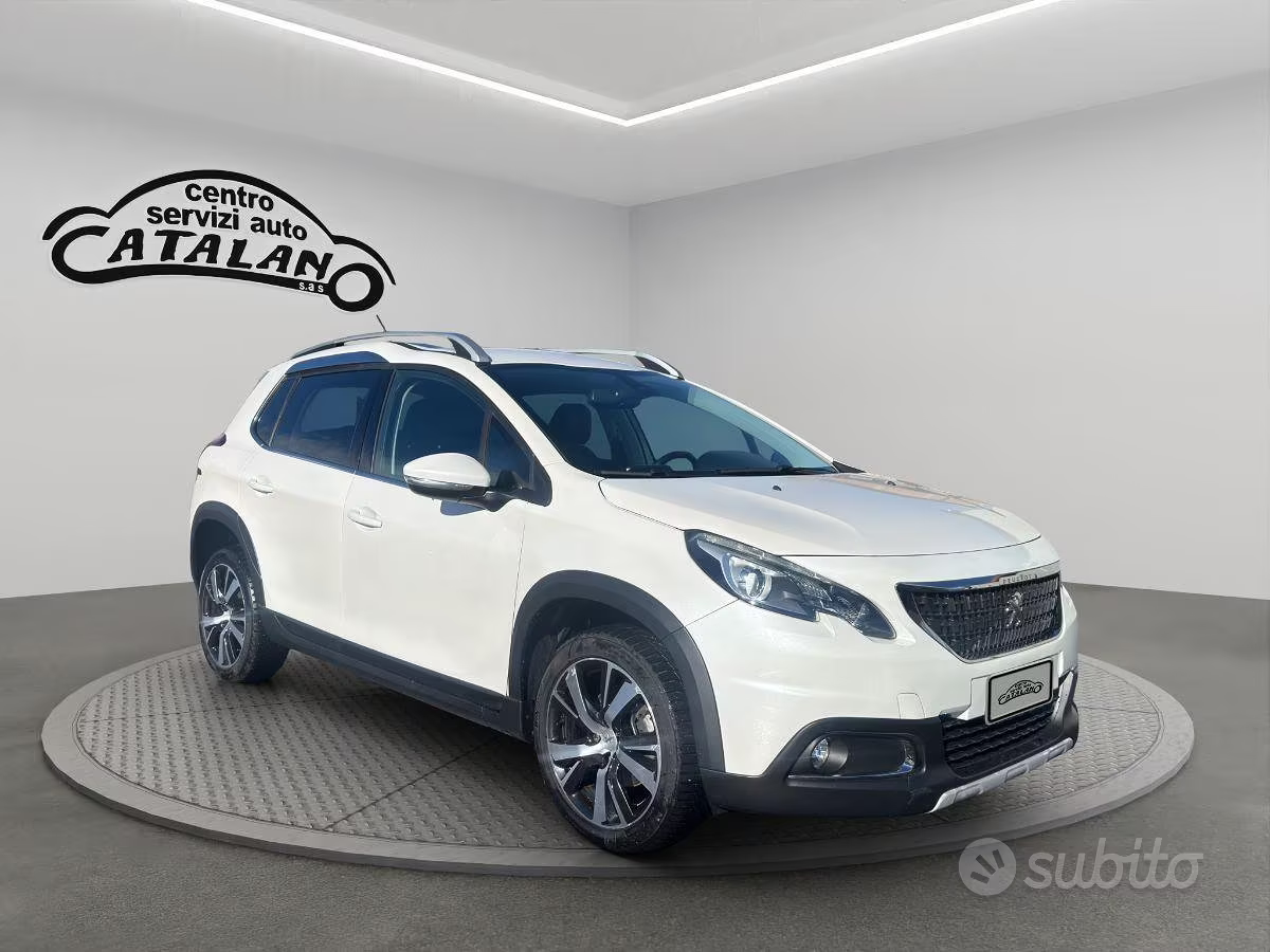 SUV bianco su piattaforma girevole in uno showroom, con il logo Catalano sulla parete.