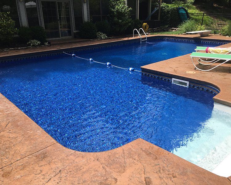 Blue swimming pool with brown concrete border; lounge chairs and diving board visible.