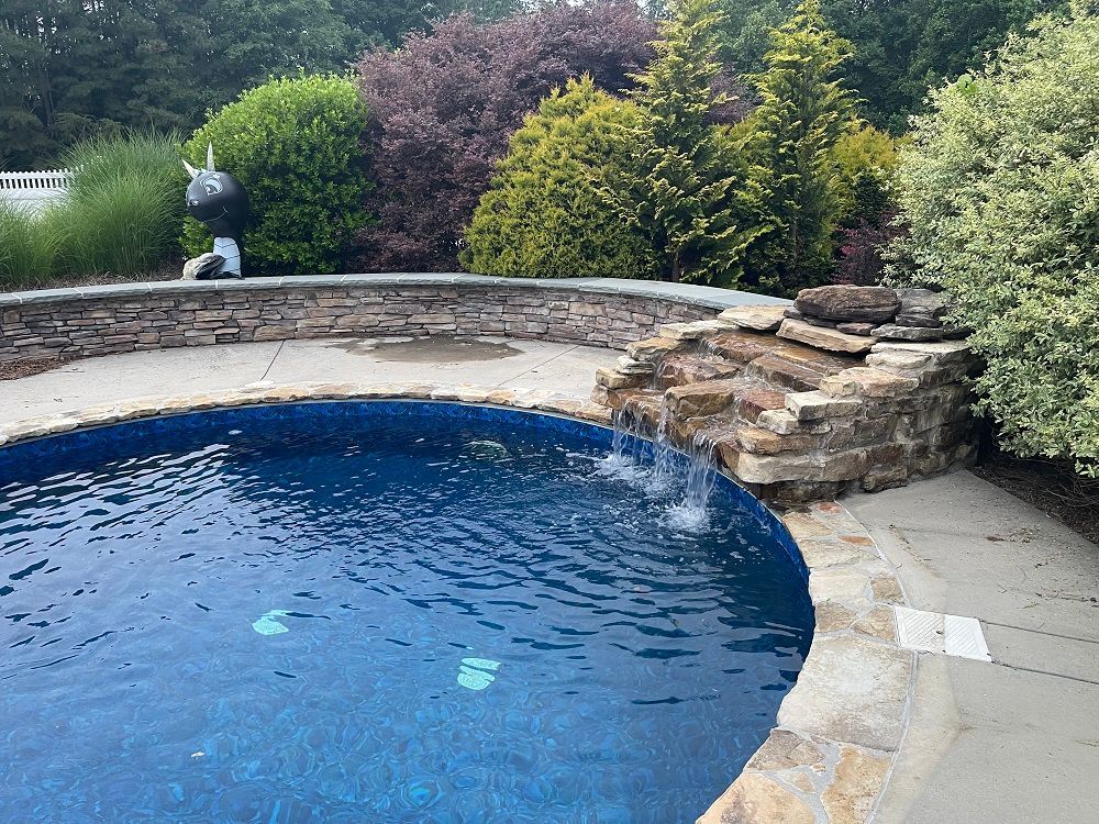 Swimming pool with stone waterfall, surrounded by landscaping and stone patio.