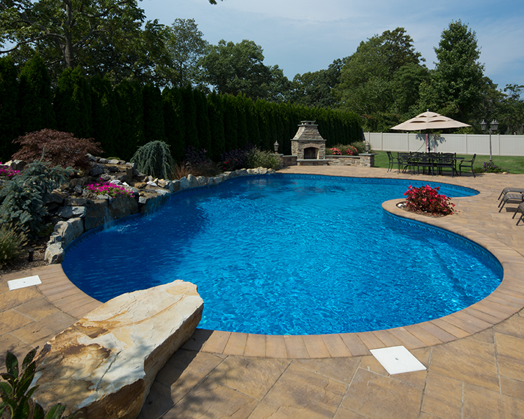 Swimming pool with stone patio, waterfall, and outdoor fireplace on a sunny day.