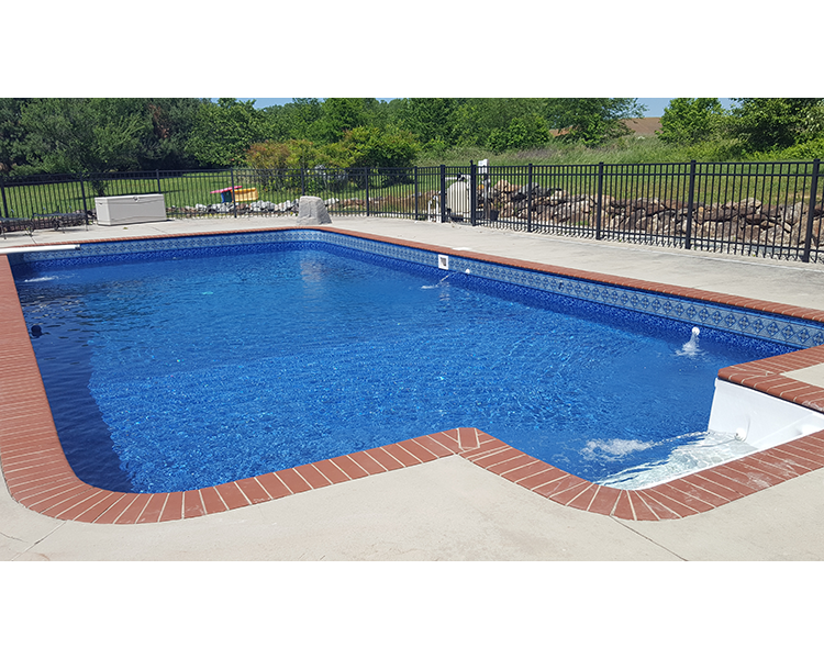 Rectangular in-ground swimming pool with brick coping and blue tile border. Black fence, concrete deck.