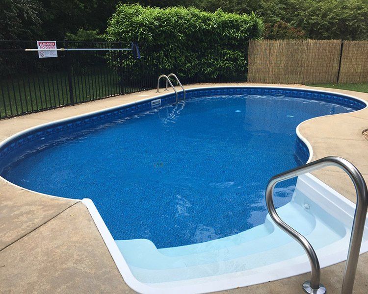 A blue, kidney-shaped swimming pool with concrete edges and metal handrails.