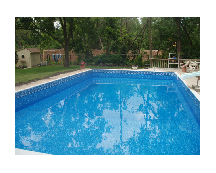 A rectangular swimming pool filled with blue water, surrounded by green grass and trees, a shed in the background.