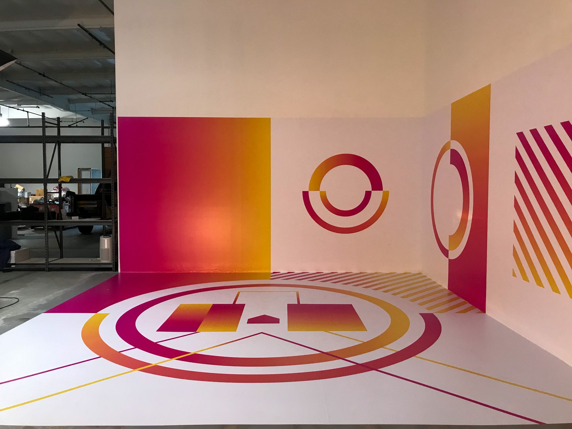 Interior space with white walls and floor, decorated with pink, orange, and yellow geometric designs.