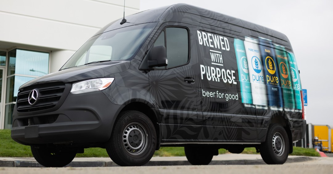 Black van with “Brewed With Purpose” branding wrapped on it, parked outside a building.