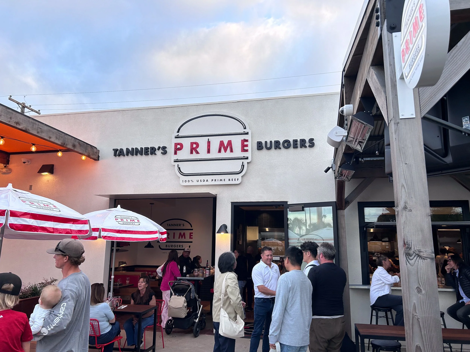 Outdoor patio of “Prime Burgers” restaurant with people dining under umbrellas at dusk