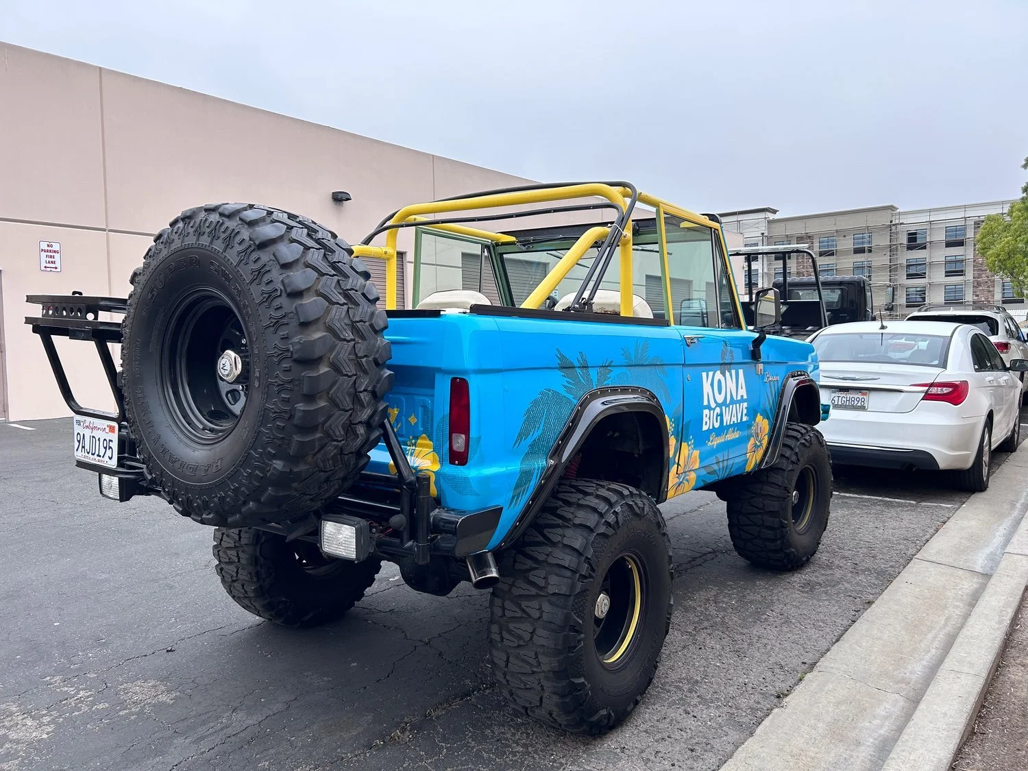 Blue vintage Bronco with yellow roll cage and large off-road tires, parked on street.