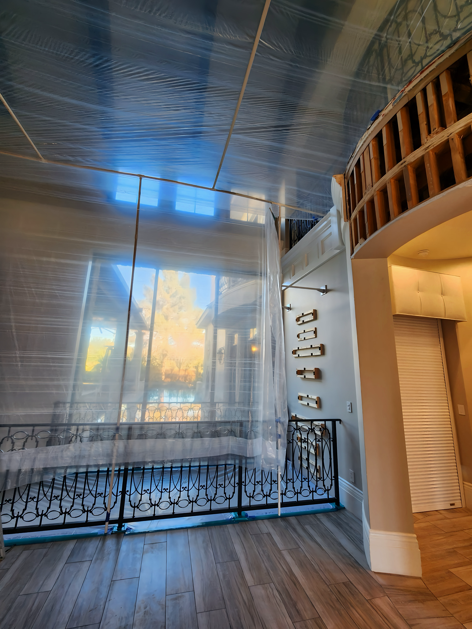 Interior view with a balcony, ornate railing, and large window with protective plastic sheeting.