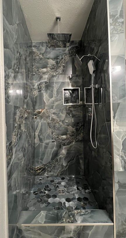A walk-in shower with dark blue and gray marbled tile. The floor is made of dark, smooth stones.