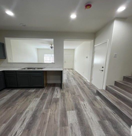 Interior view of a kitchen with dark gray cabinets, open to a hallway with wood-look flooring.