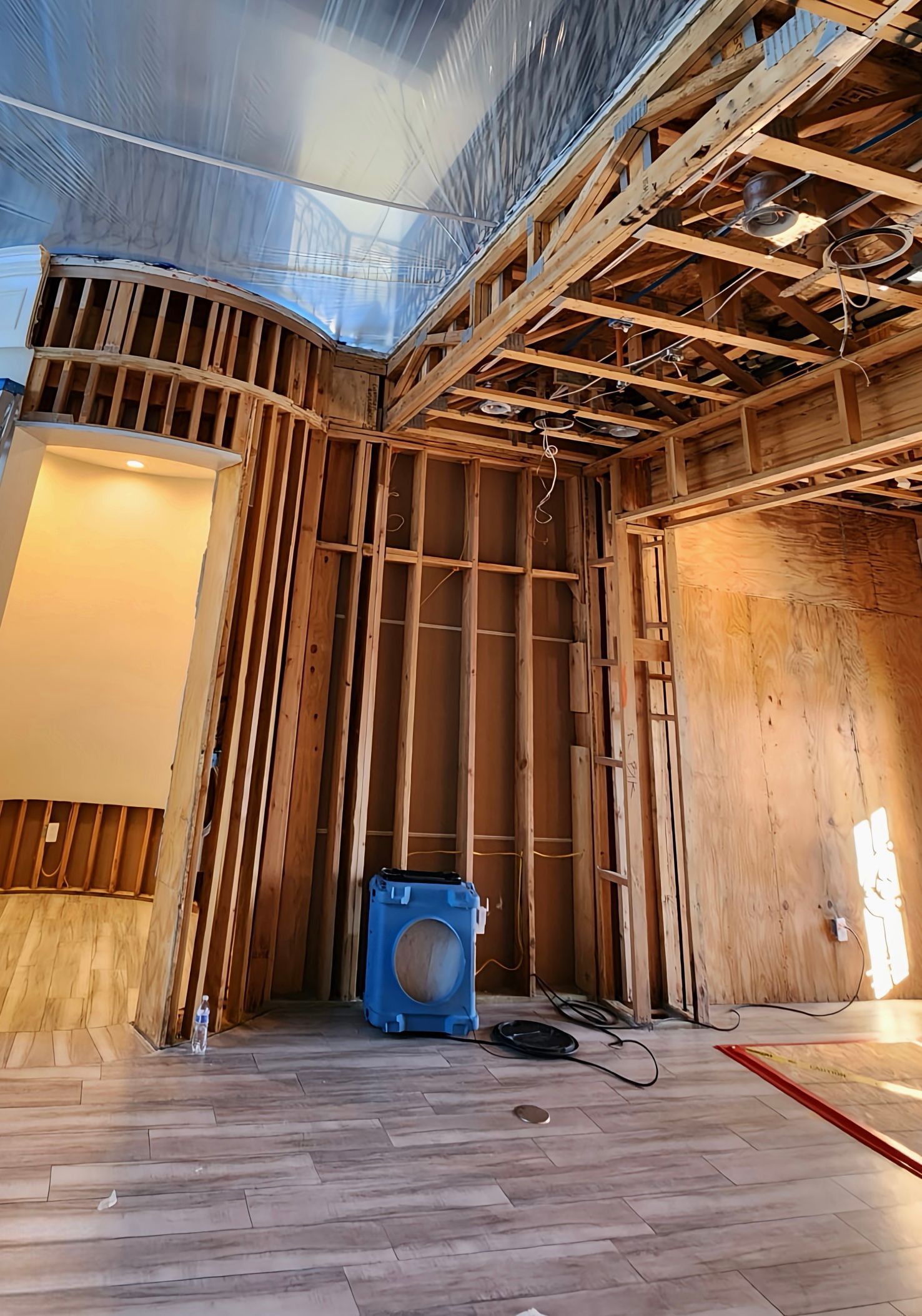 Interior construction site with exposed wooden framing and a blue dehumidifier.