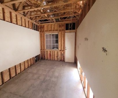 Interior view of a room under construction. Bare wooden studs are visible, with drywall partially installed on the walls.