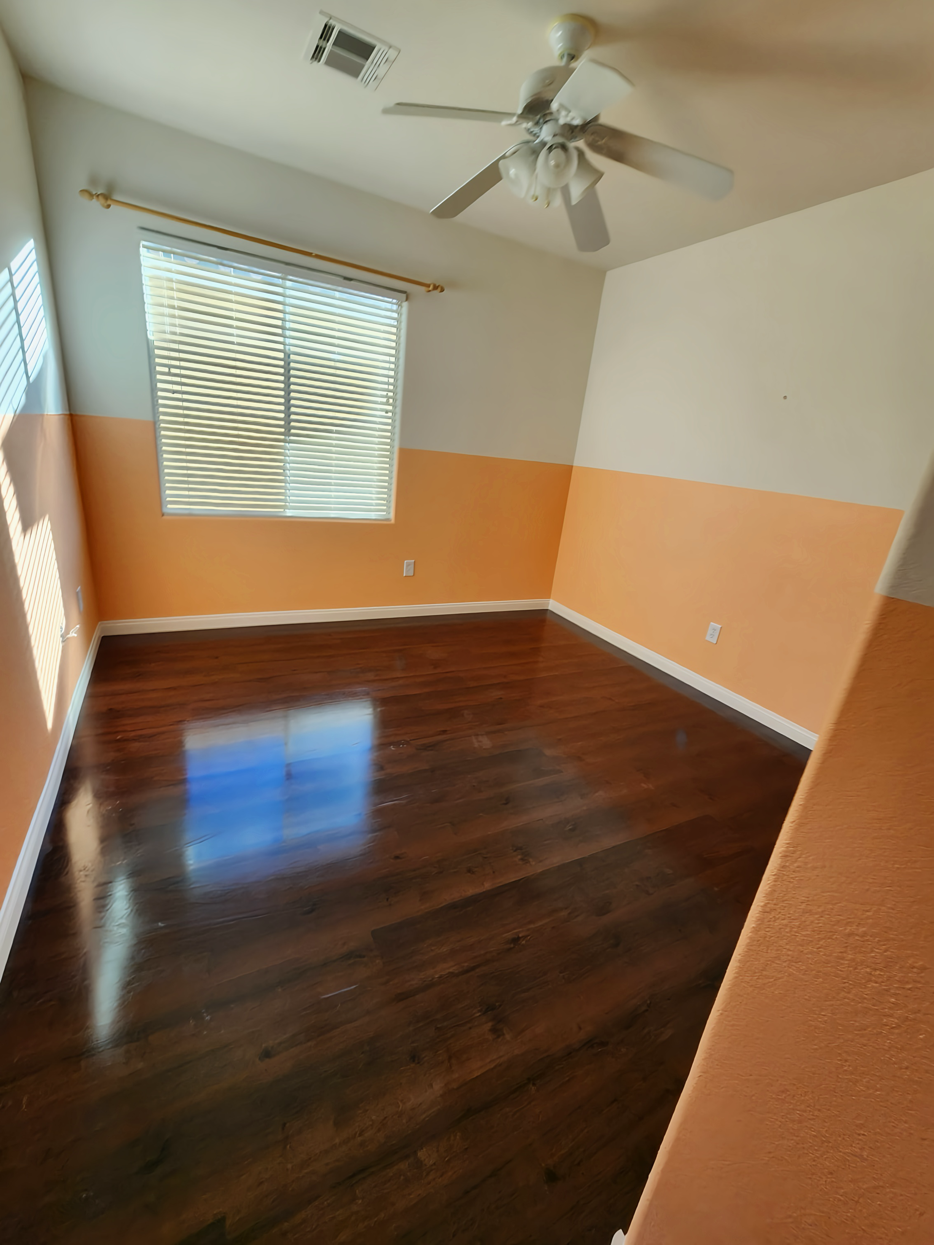 Empty room with dark wood floor, tan and orange walls, and a ceiling fan.