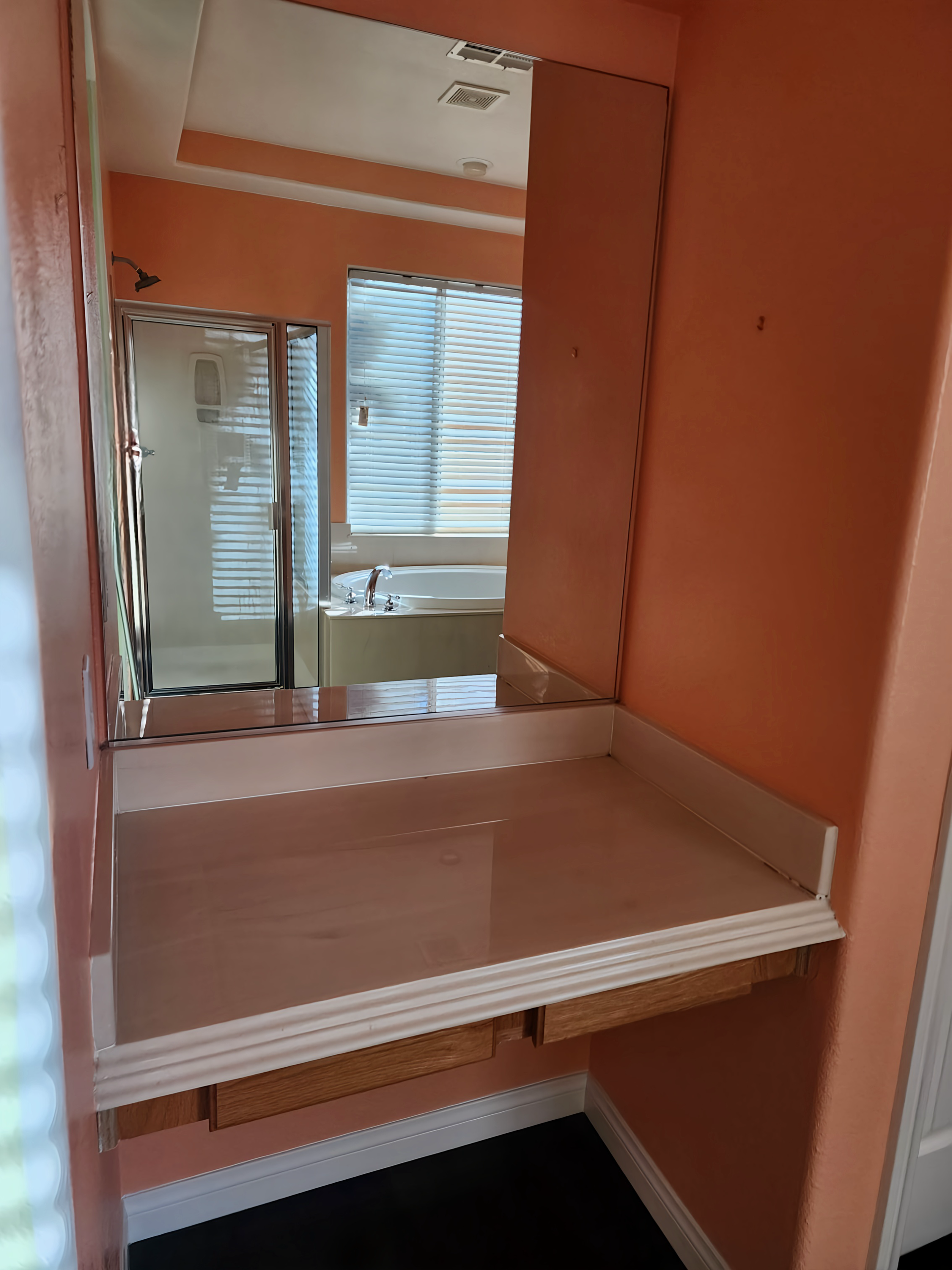 Vanity area with a mirror and counter against an orange wall. Window visible in the mirror's reflection.