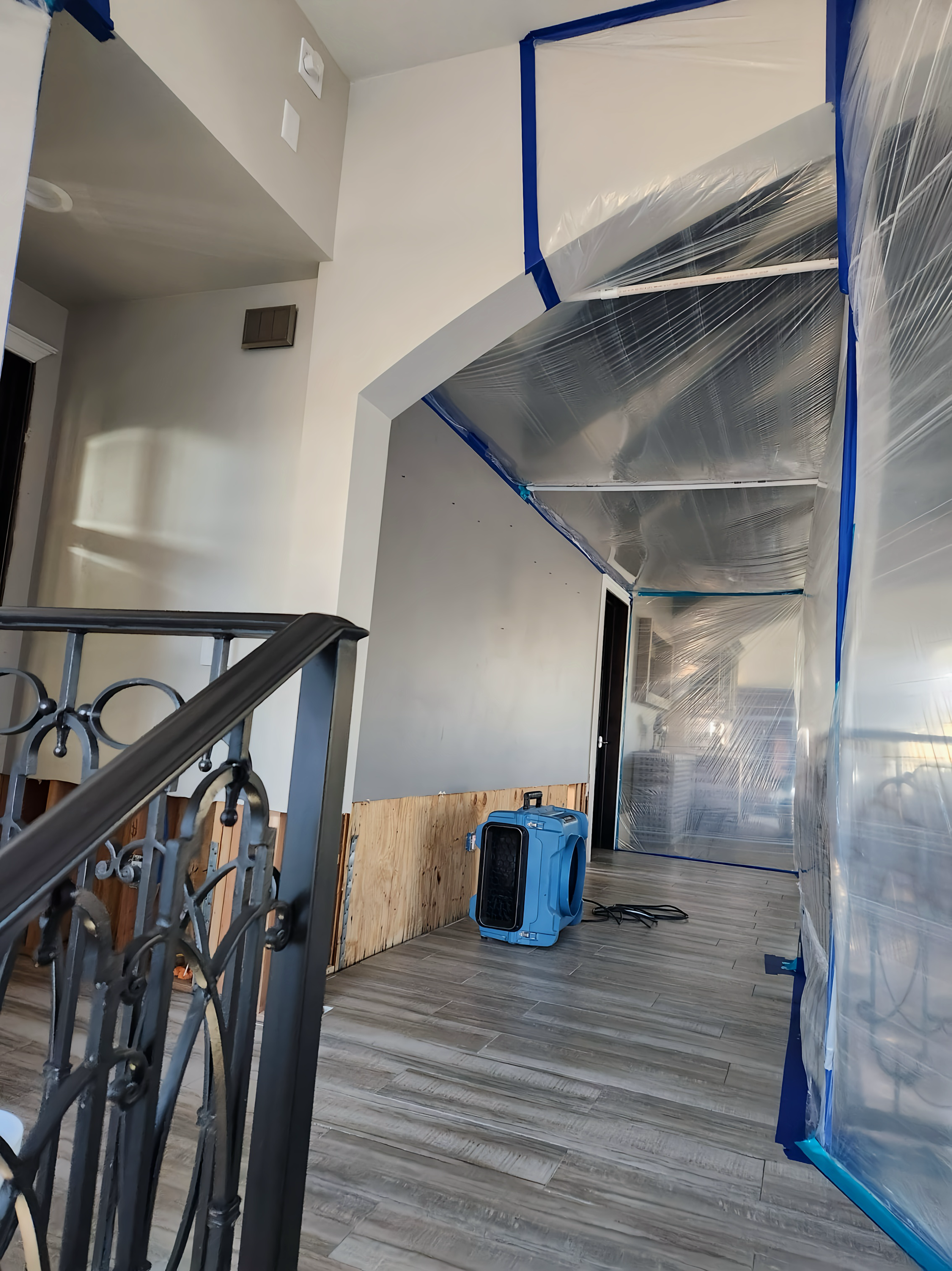 Hallway with plastic sheeting and dehumidifier, possibly for flood or mold remediation.