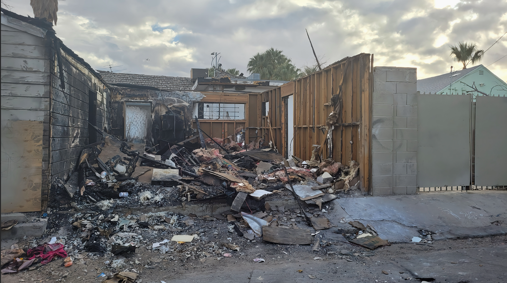 Charred remains of a building, debris piled in front. Sky overhead.