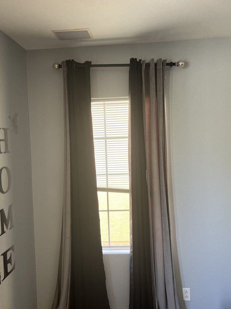 A bedroom with a window and curtains and a sign on the wall that says home.