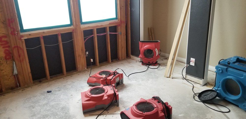 Three red fans are sitting on the floor of a room in a house under construction.