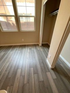 A bedroom with hardwood floors , a closet and two windows.