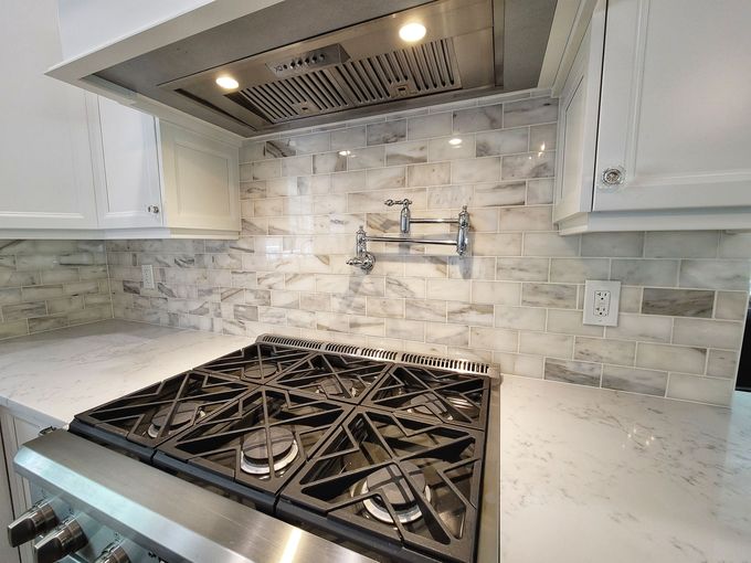Modern kitchen with stainless gas range, white cabinets, marble backsplash, and under-cabinet lighting
