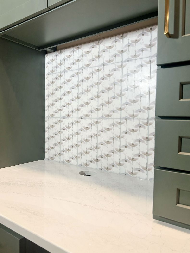 Empty desk nook with gray cabinets and drawers against a patterned white backsplash