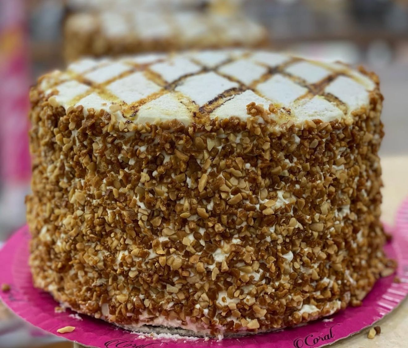 Pastel redondo con lados cubiertos de nueces, parte superior con patrón de diamantes y base de papel rosa.