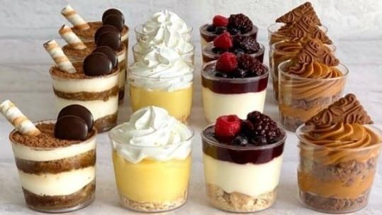 Tazas de postre con rellenos y coberturas en capas, que incluyen crema batida, bayas y chocolate.