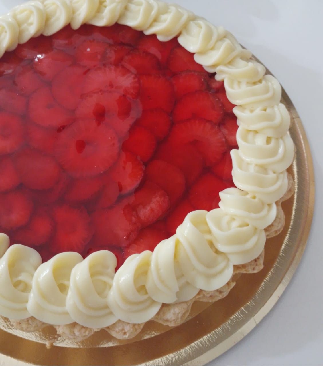 Tarta de fresas con borde de glaseado blanco sobre plato dorado.