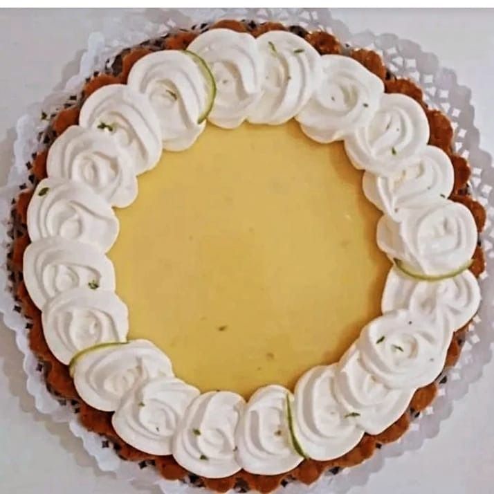 Tarta de lima con borde de crema batida sobre un tapete blanco.