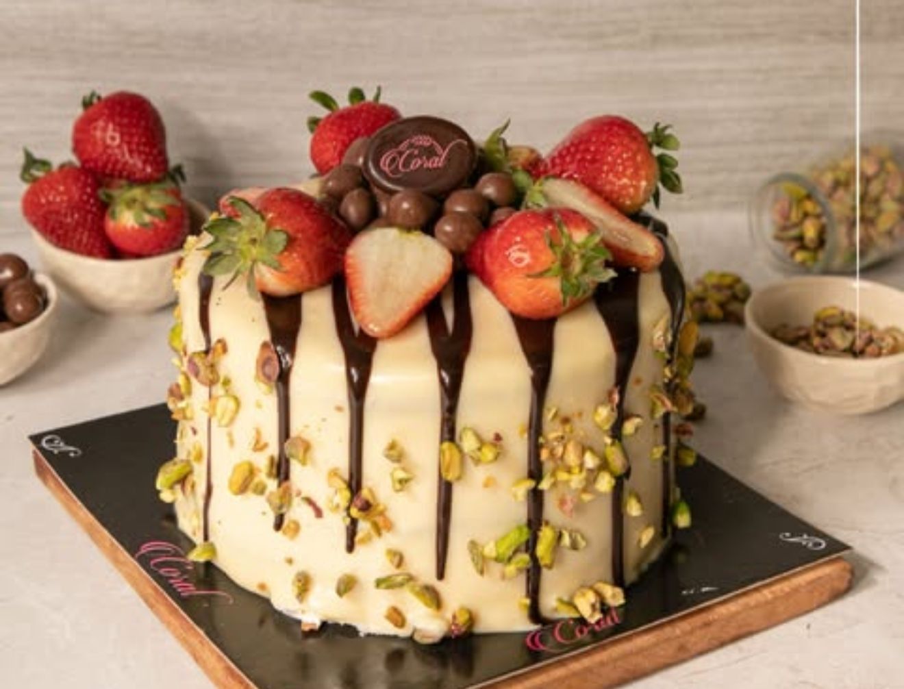 Pastel decorado con fresas, llovizna de chocolate y pistachos sobre una tabla de madera.