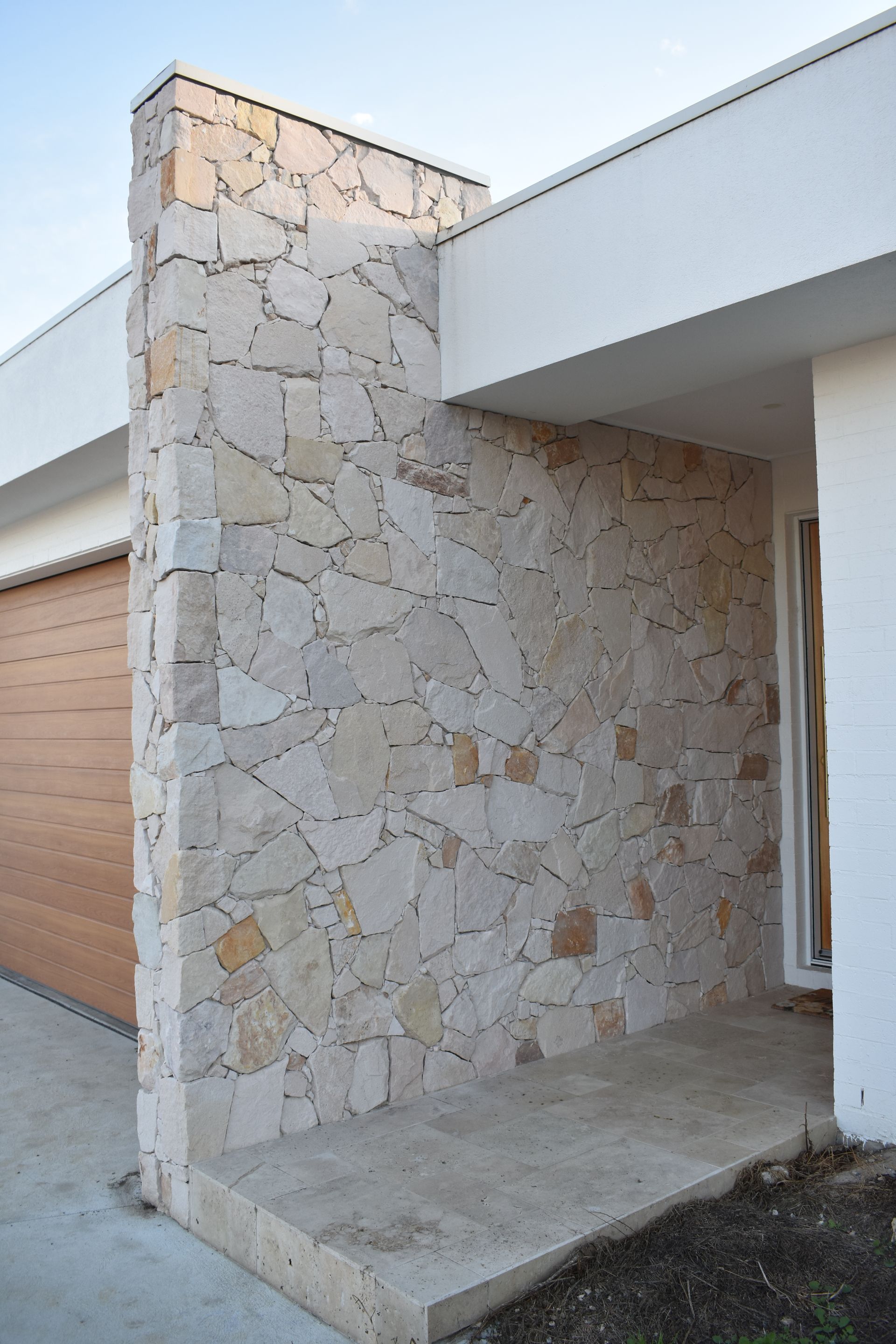Stone-clad exterior entryway with a covered concrete porch and white roof overhang