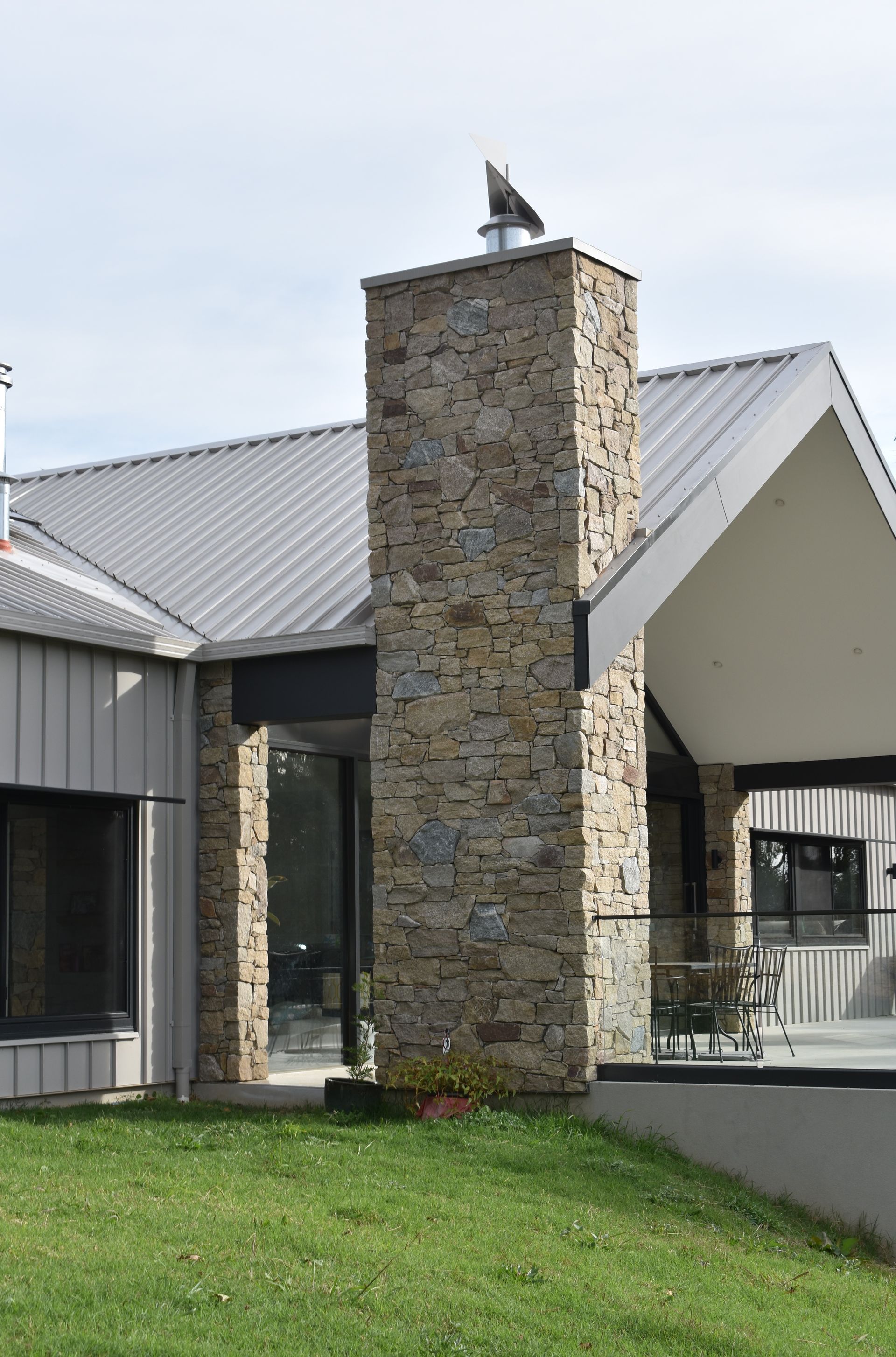 Stone chimney on a modern house with a metal roof and grassy foreground