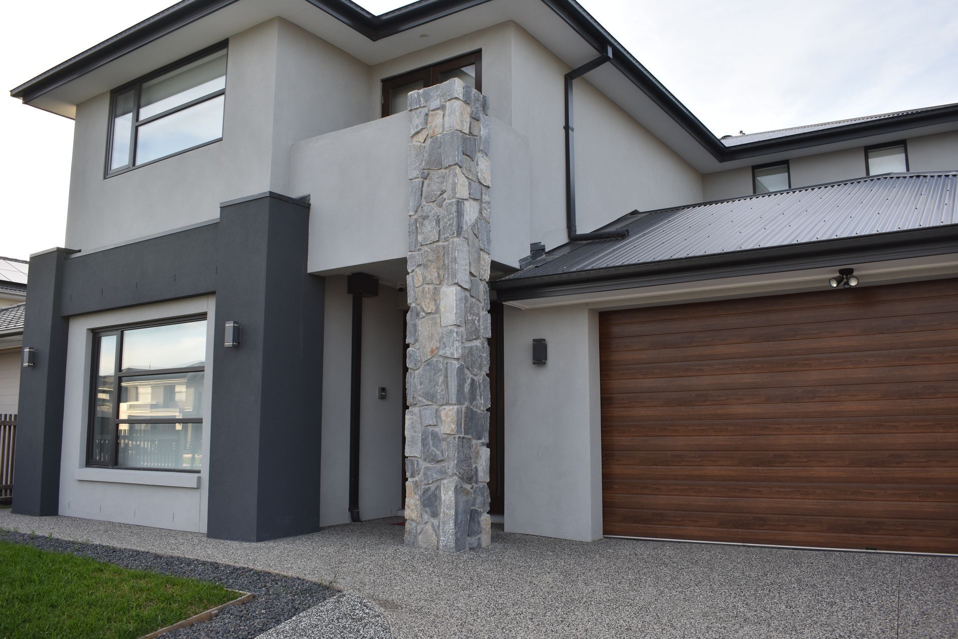 Modern two-story house exterior with gray stone accents and a wooden garage door