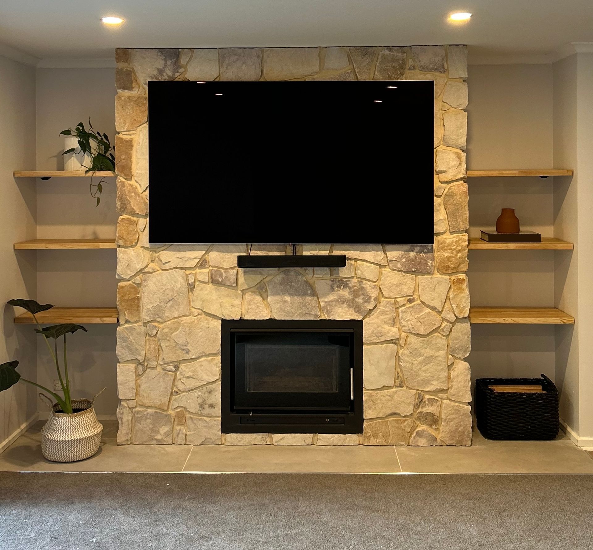 Stone fireplace wall with mounted TV, built-in shelves, and a black fireplace insert in a living room