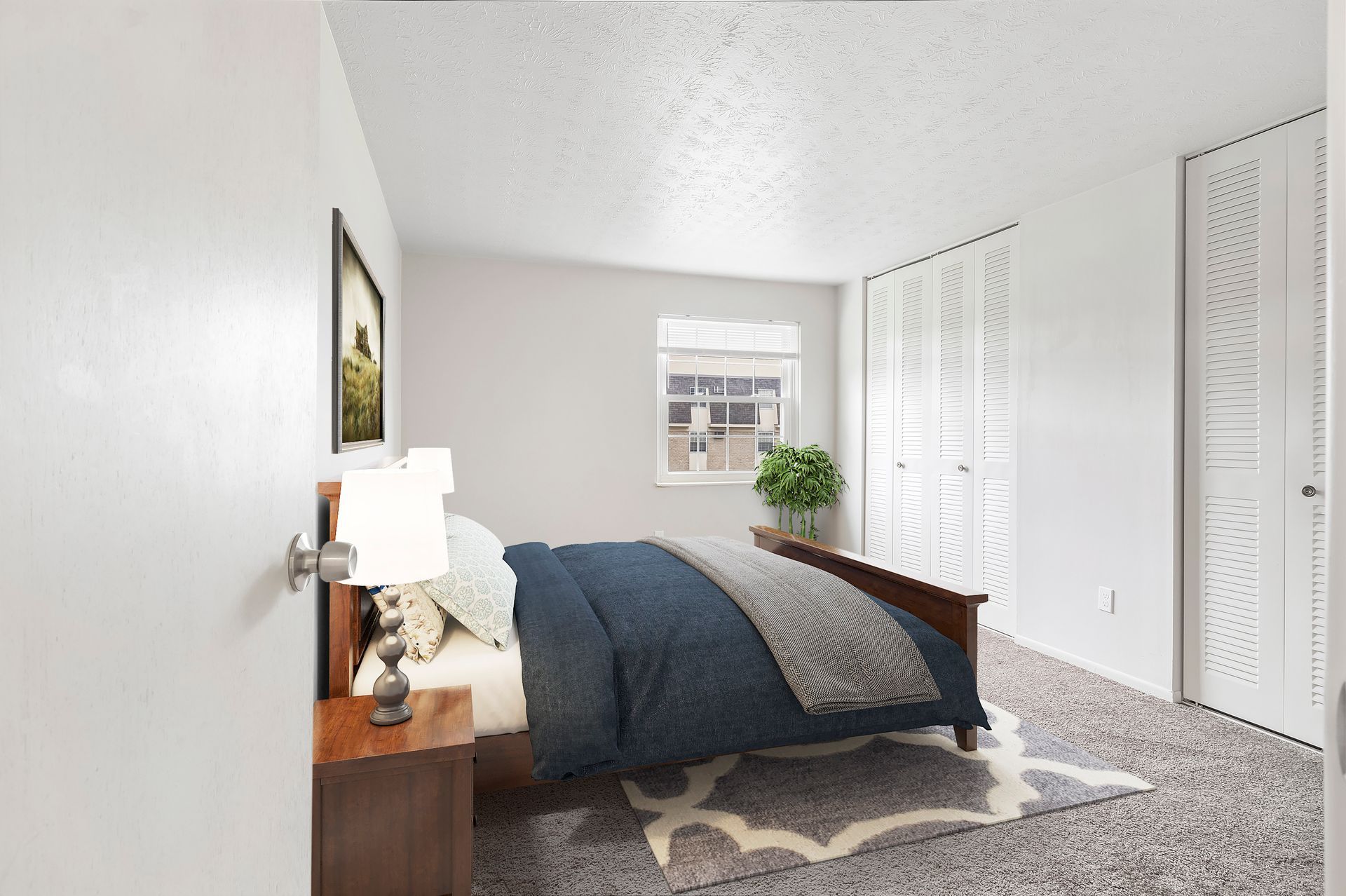 A bedroom with a bed , nightstand , lamp and window.