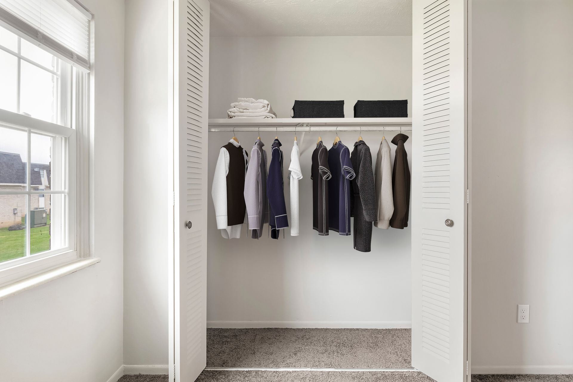 A walk in closet with clothes hanging in it and a window.