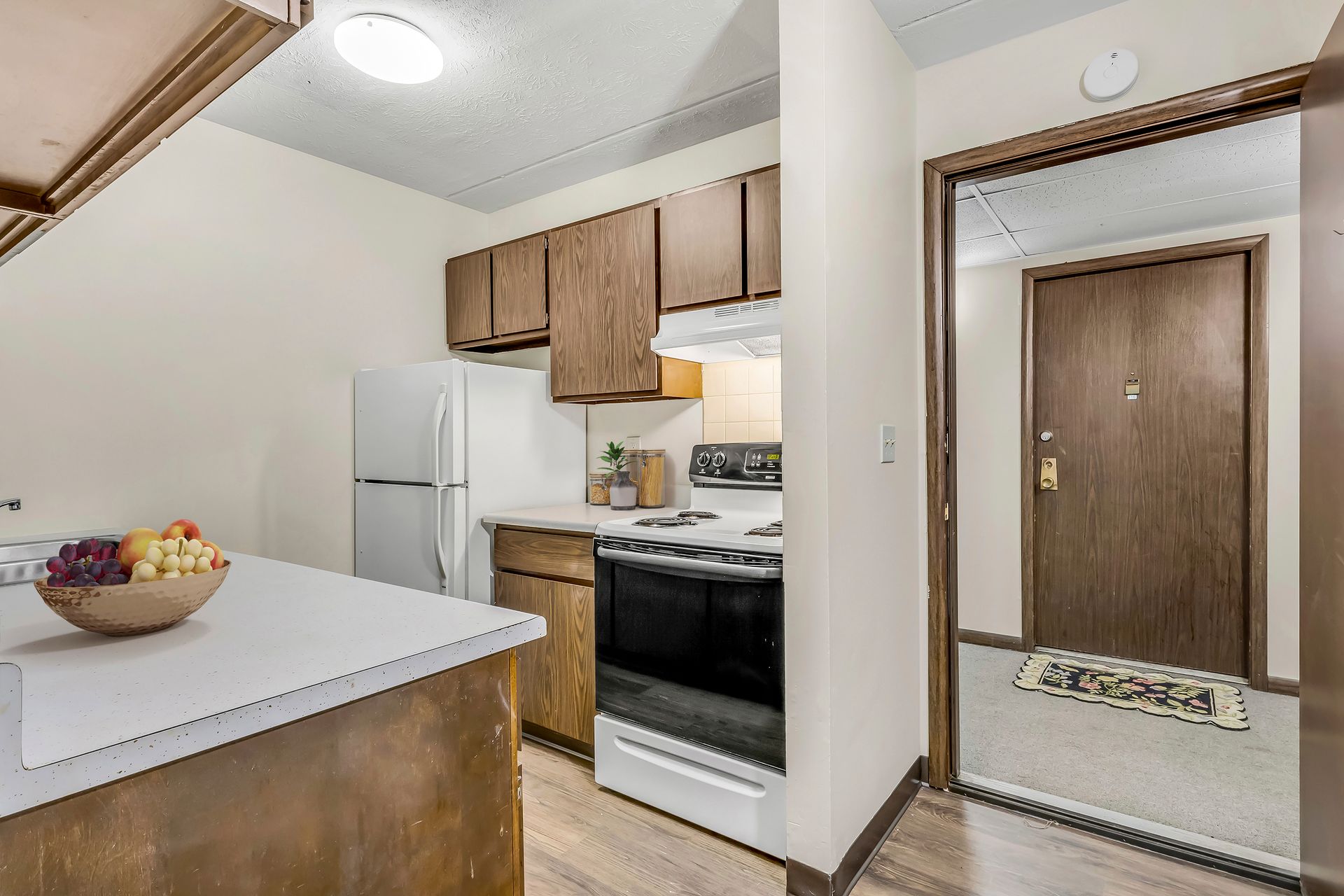 A kitchen with a bowl of fruit on the counter and a refrigerator.