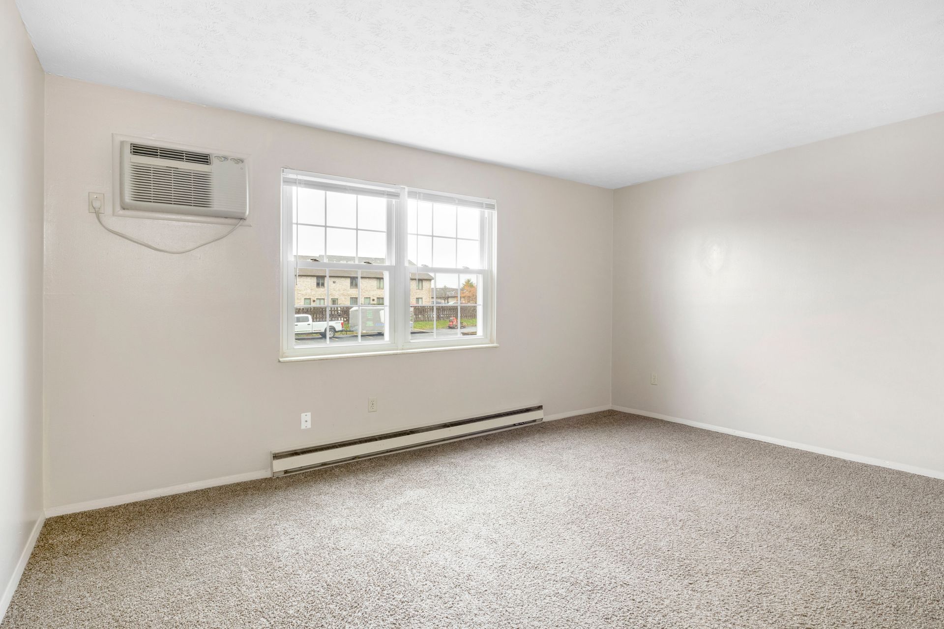 An empty living room with a window and air conditioner.