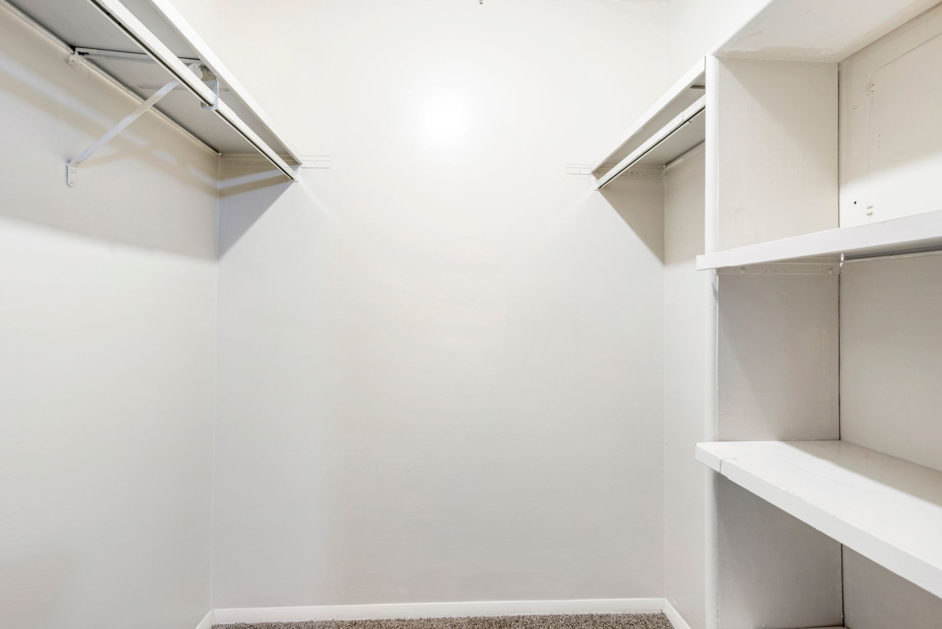 An empty walk in closet with white shelves and clothes racks.