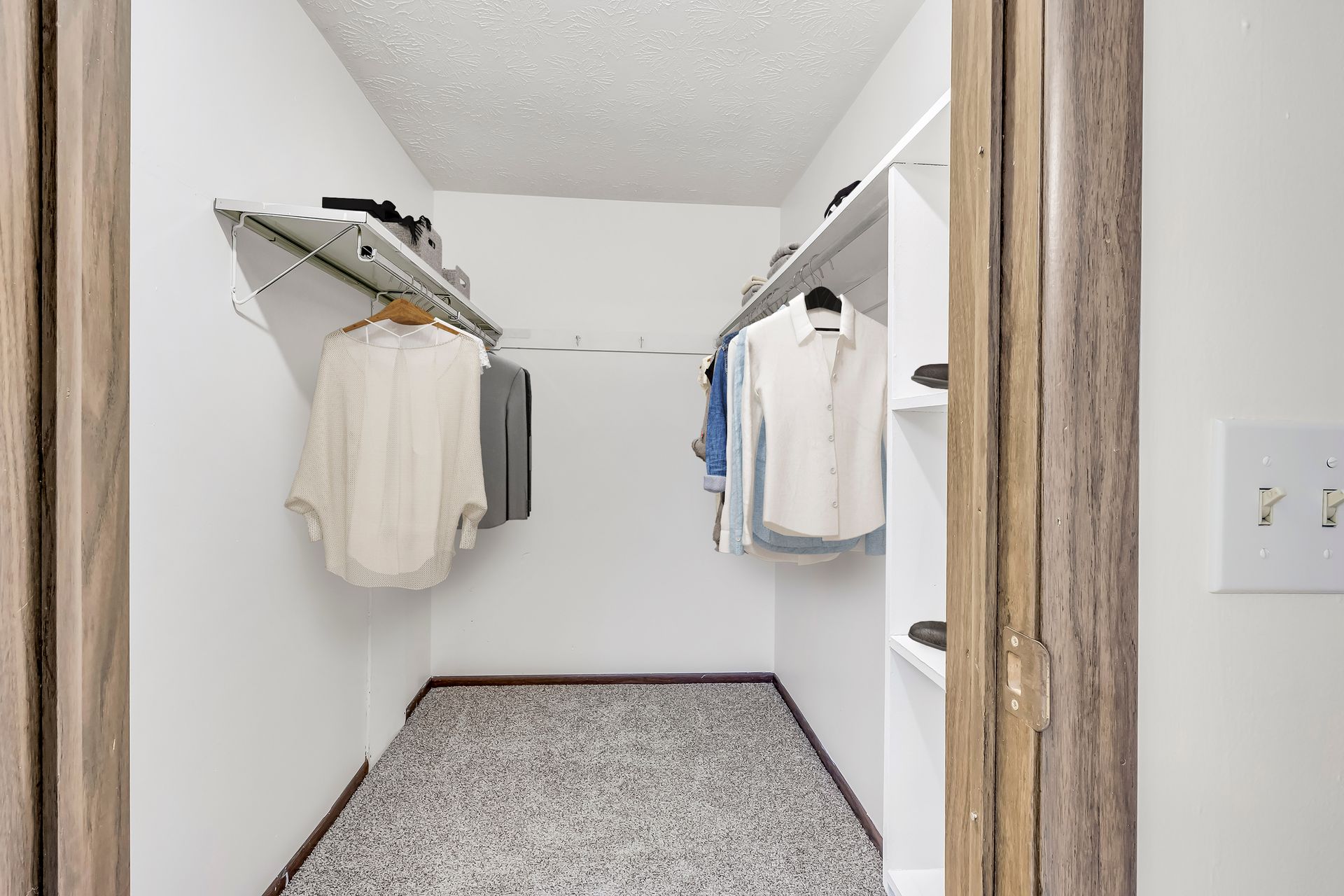 A walk in closet with clothes hanging on shelves and a door.