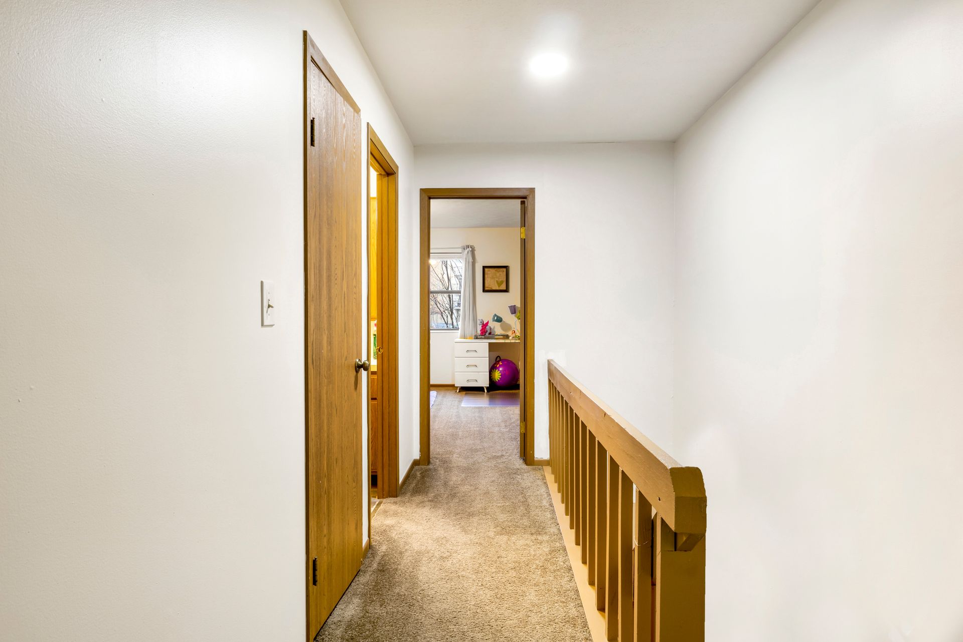 A hallway in a house with a wooden railing leading to a bedroom.