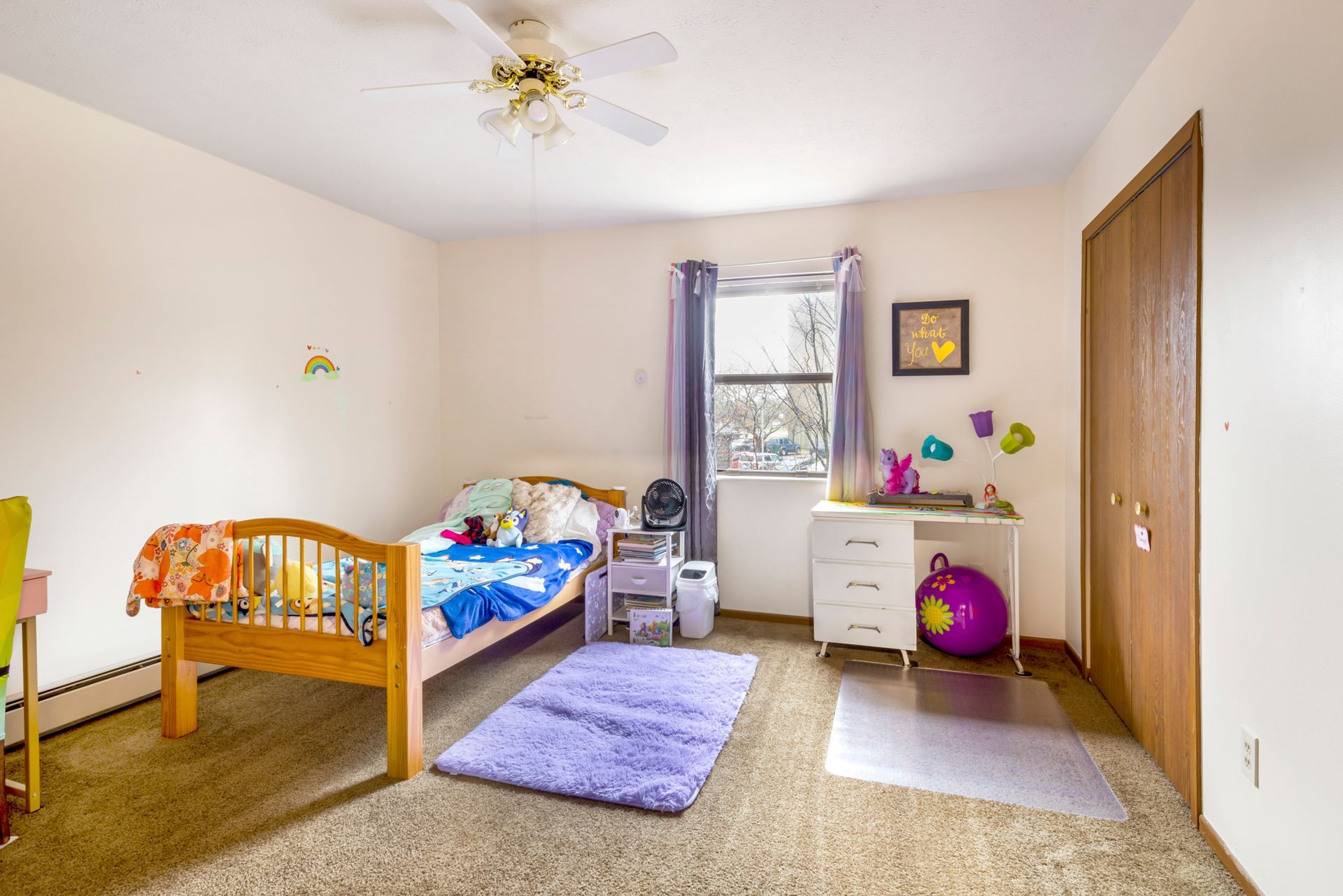 A bedroom with a bed , desk , purple rug and a ceiling fan.