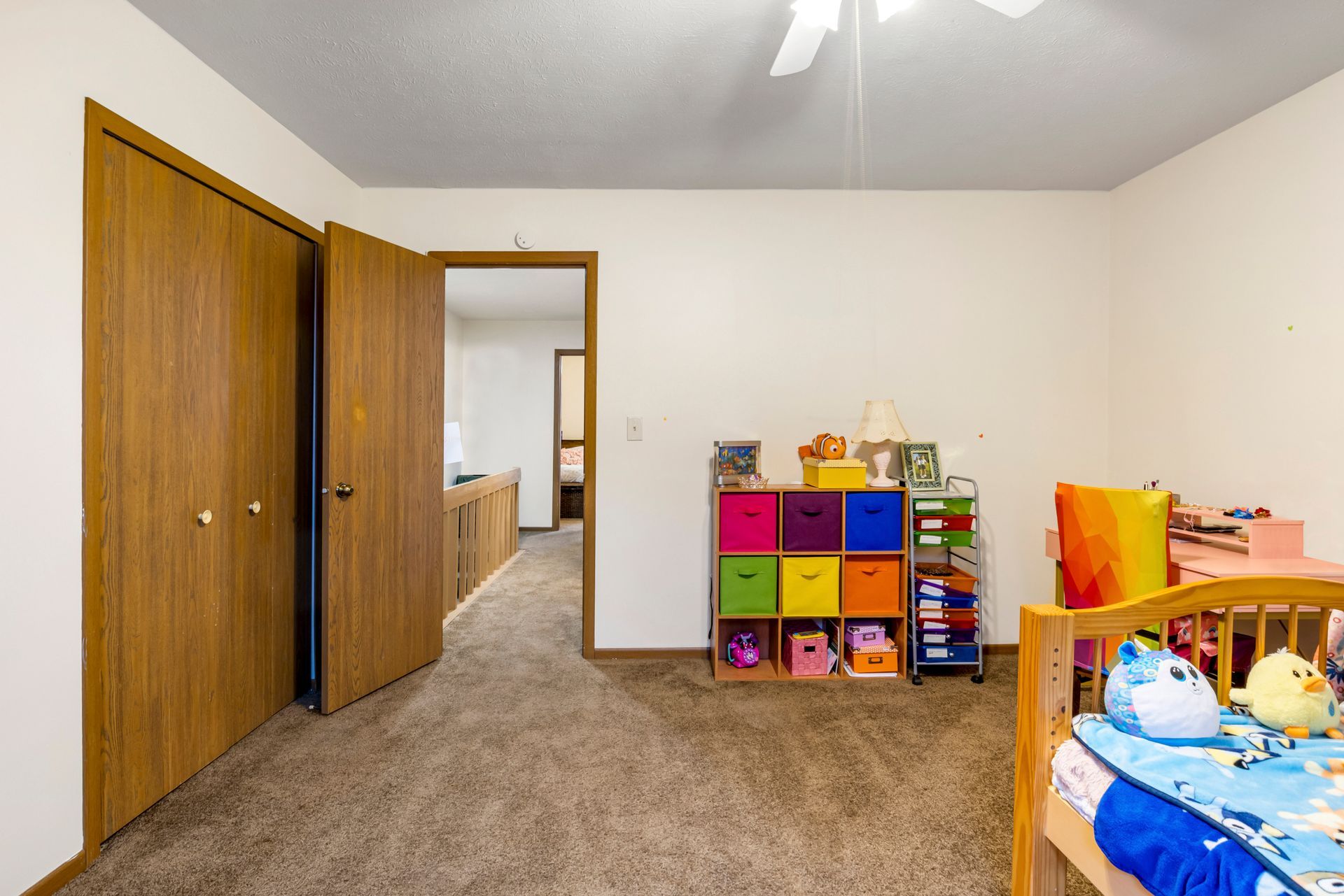 A bedroom with a crib , a shelf , and a ceiling fan.