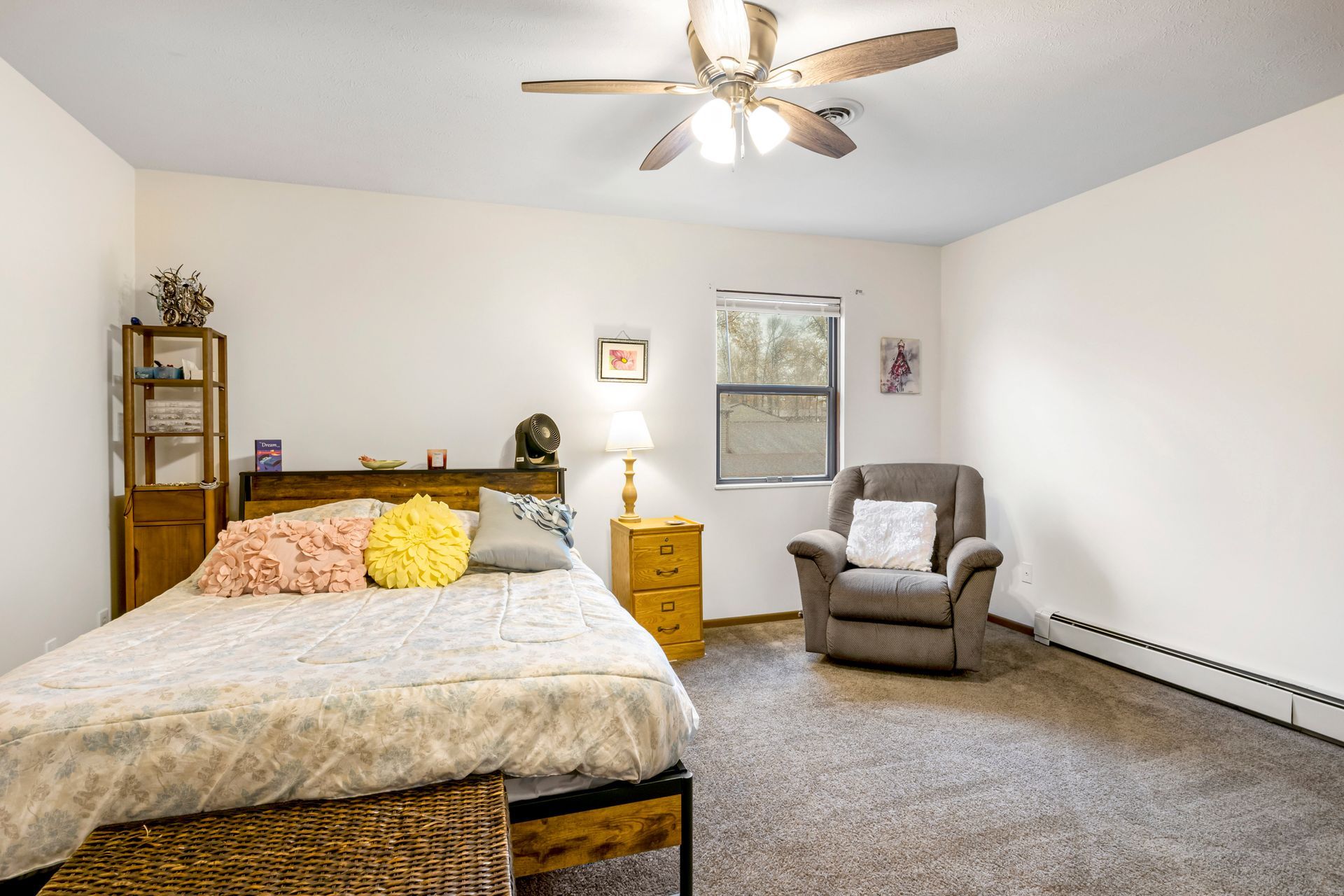 A bedroom with a bed , chair , nightstand and ceiling fan.