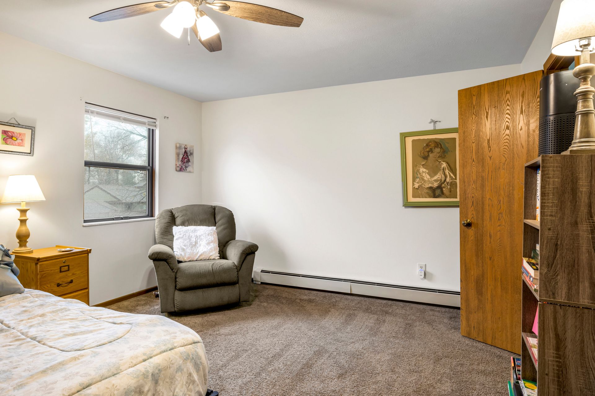 A bedroom with a bed , chair , nightstand and ceiling fan.
