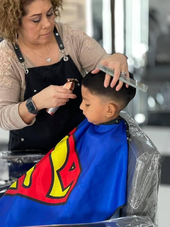 A woman is cutting a young boy 's hair in a salon.