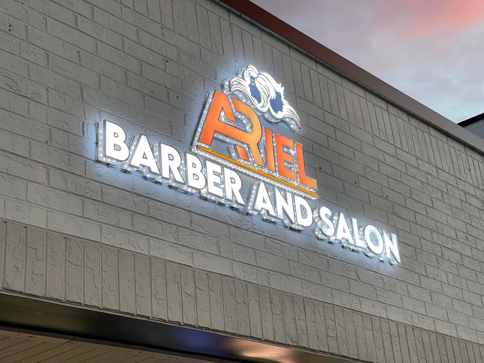 A barber and salon sign is lit up on the side of a building