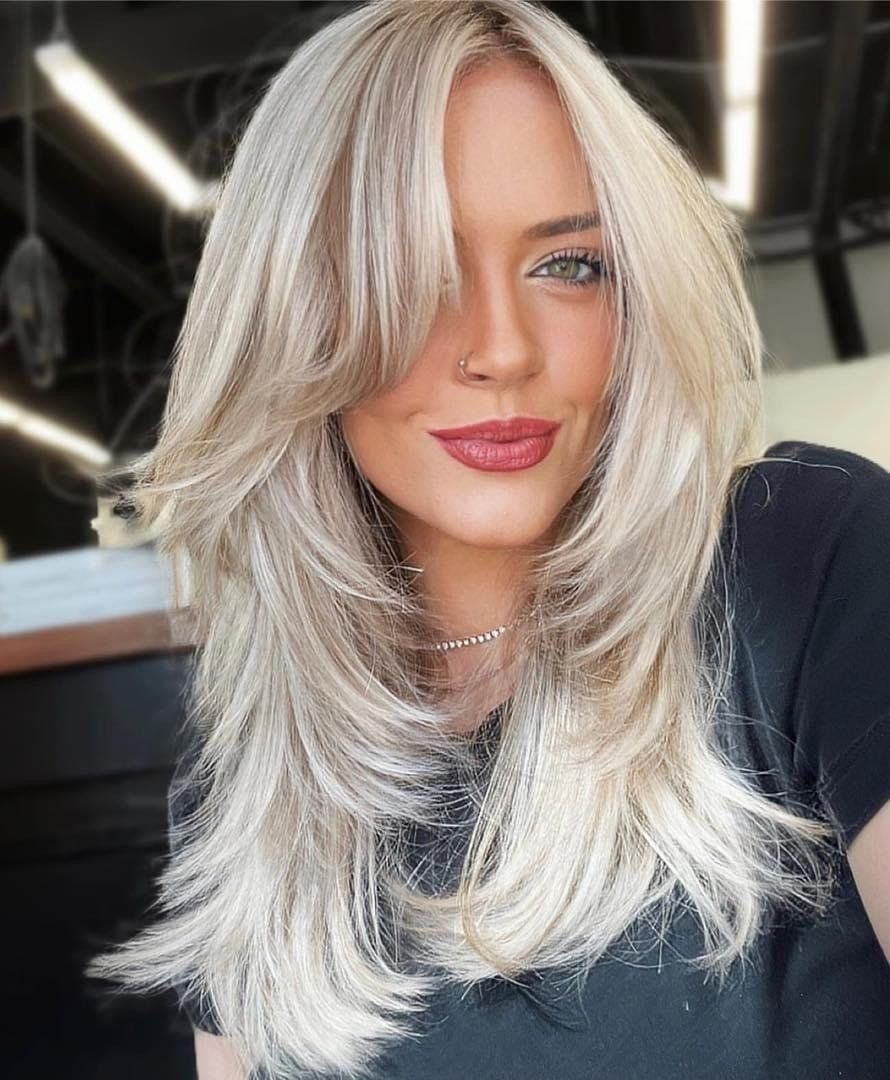 A woman with long blonde hair is wearing a black shirt and a necklace.