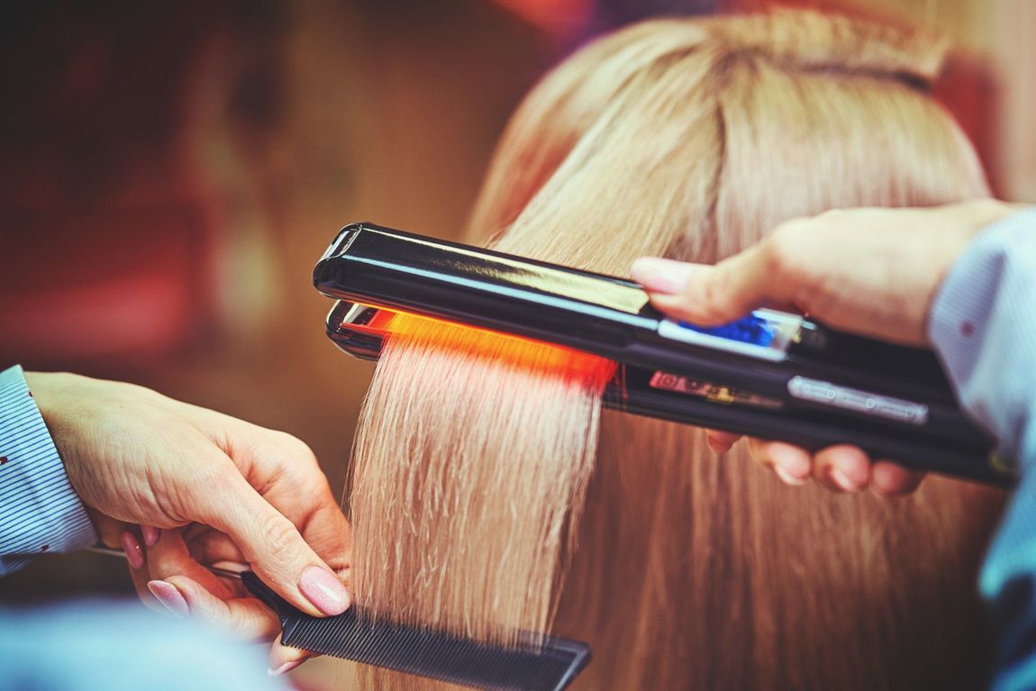 A woman is getting her hair straightened by a hairdresser.