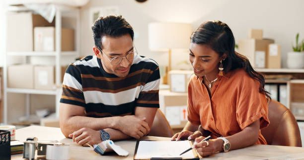 A man and a woman are sitting at a table looking at a clipboard.